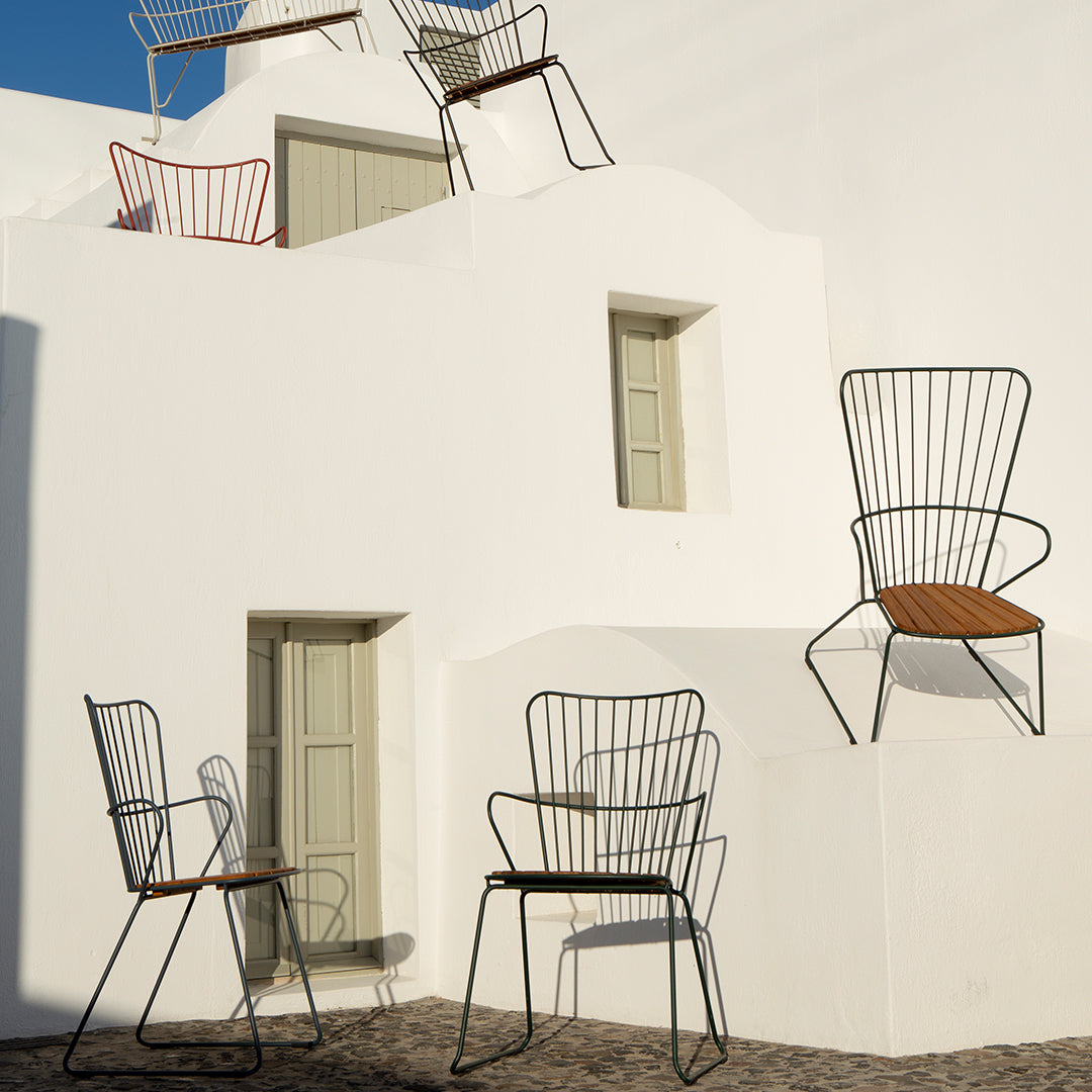 "Colorful wire chairs in red, white, and black with wooden seats against a minimalistic white wall backdrop."