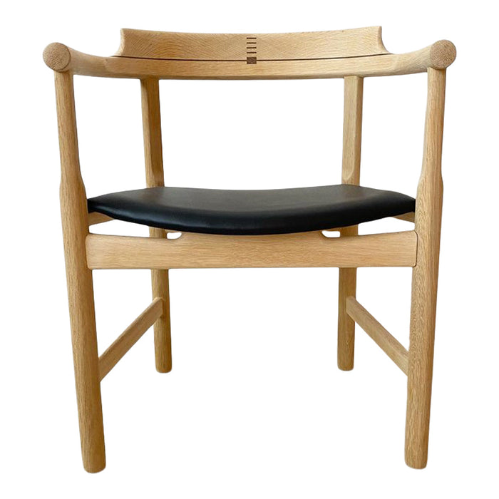 Natural wood chair with a light oak finish and a sleek black leather seat, featuring minimalistic design.