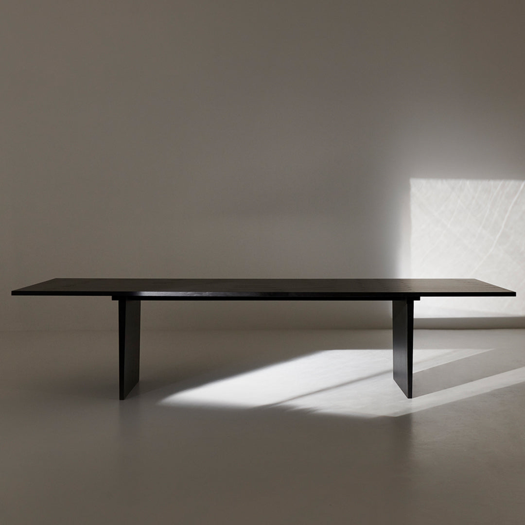 Elegant black rectangular dining table with smooth surface and minimalist design, set against a light backdrop.