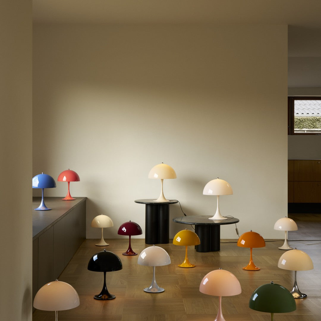 Collection of colorful Panthella table lamps on a wooden floor against a beige wall.