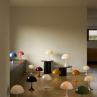 Collection of colorful Panthella table lamps on a wooden floor against a beige wall.