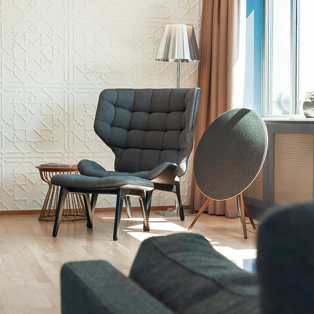 Gray tufted armchair and matching ottoman in a bright, modern interior with warm wood tones and soft light.