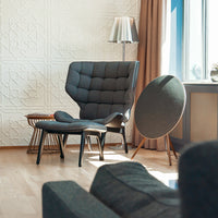 Gray tufted armchair and matching ottoman in a bright, modern interior with warm wood tones and soft light.