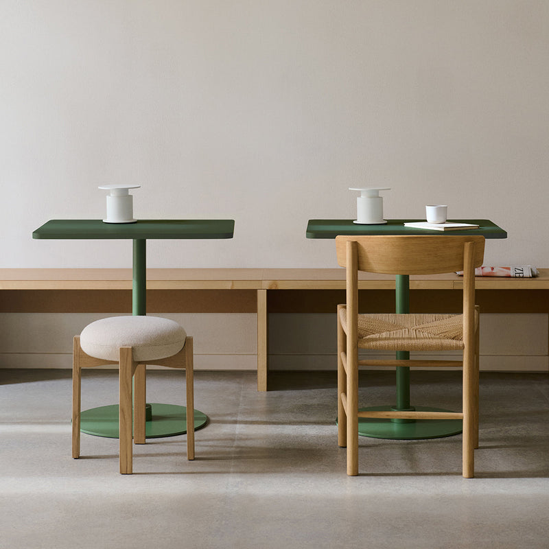 Green tabletop and base with beige upholstered stool and natural wood chairs, minimalistic design.