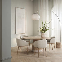 "Light beige upholstered chairs around a round wood table in a soft pastel green and natural wood setting."