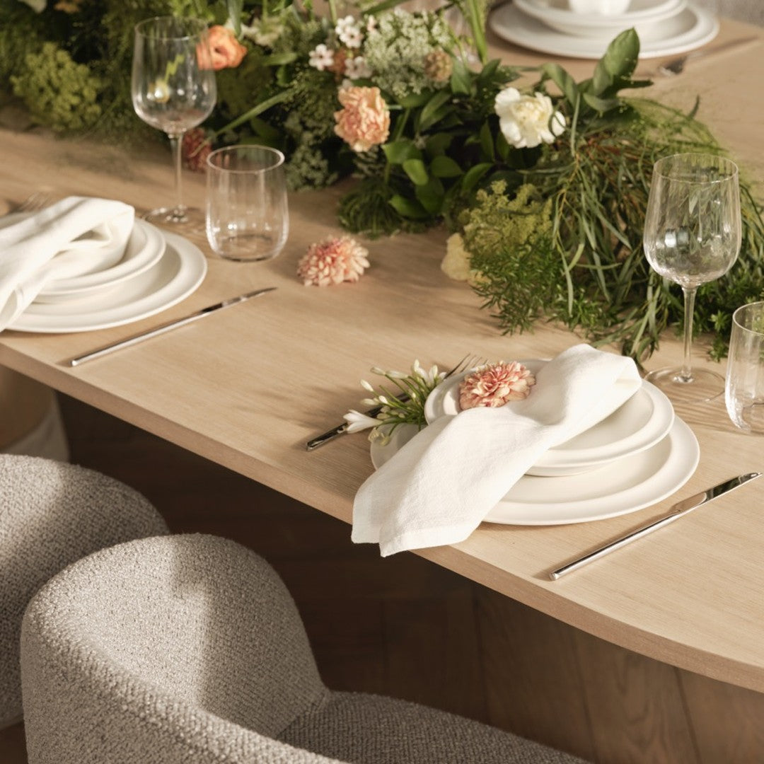 Elegant table setting with neutral tones, soft white plates, and delicate floral accents on a light wood surface.