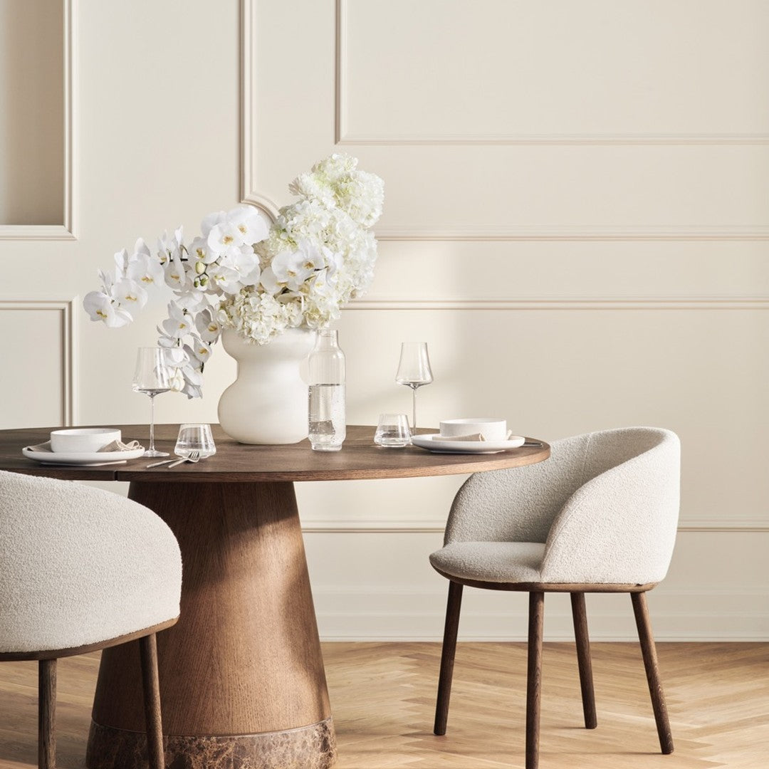 Neutral beige tones with soft textures, featuring a round wooden table and cozy cream chairs for an inviting dining setting.
