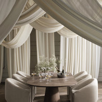 Elegant beige drapes with soft, flowing patterns create a warm, inviting atmosphere around a modern wooden dining table.