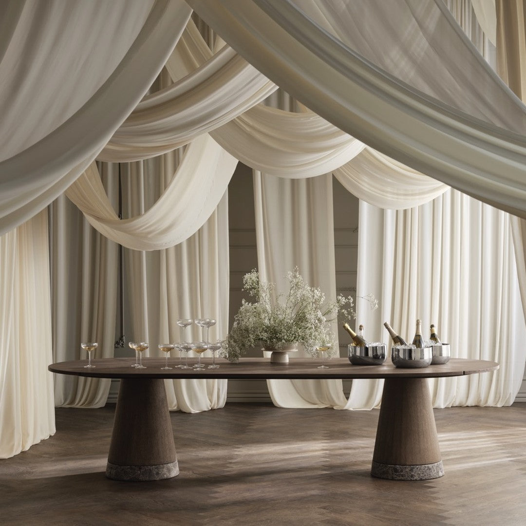 Elegant round table with smooth brown finish, set against soft cream drapery and a wooden floor. Perfect for chic events.