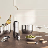 Sleek silver barware set with modern design, featuring polished metal finishes and elegant glassware on a textured brown table.