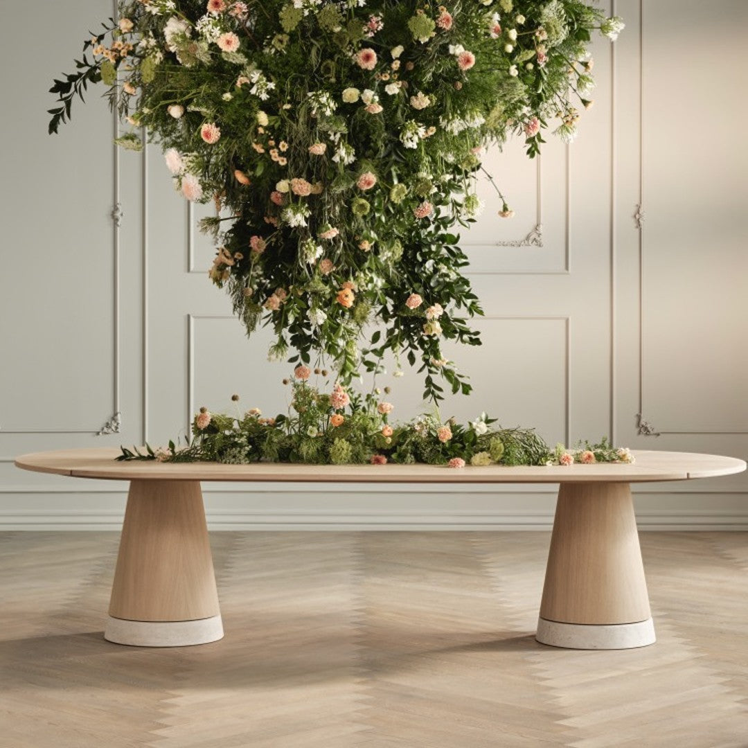 Elegant light wood table with white bases, adorned with lush greenery and blooming flowers in soft pastel colors.