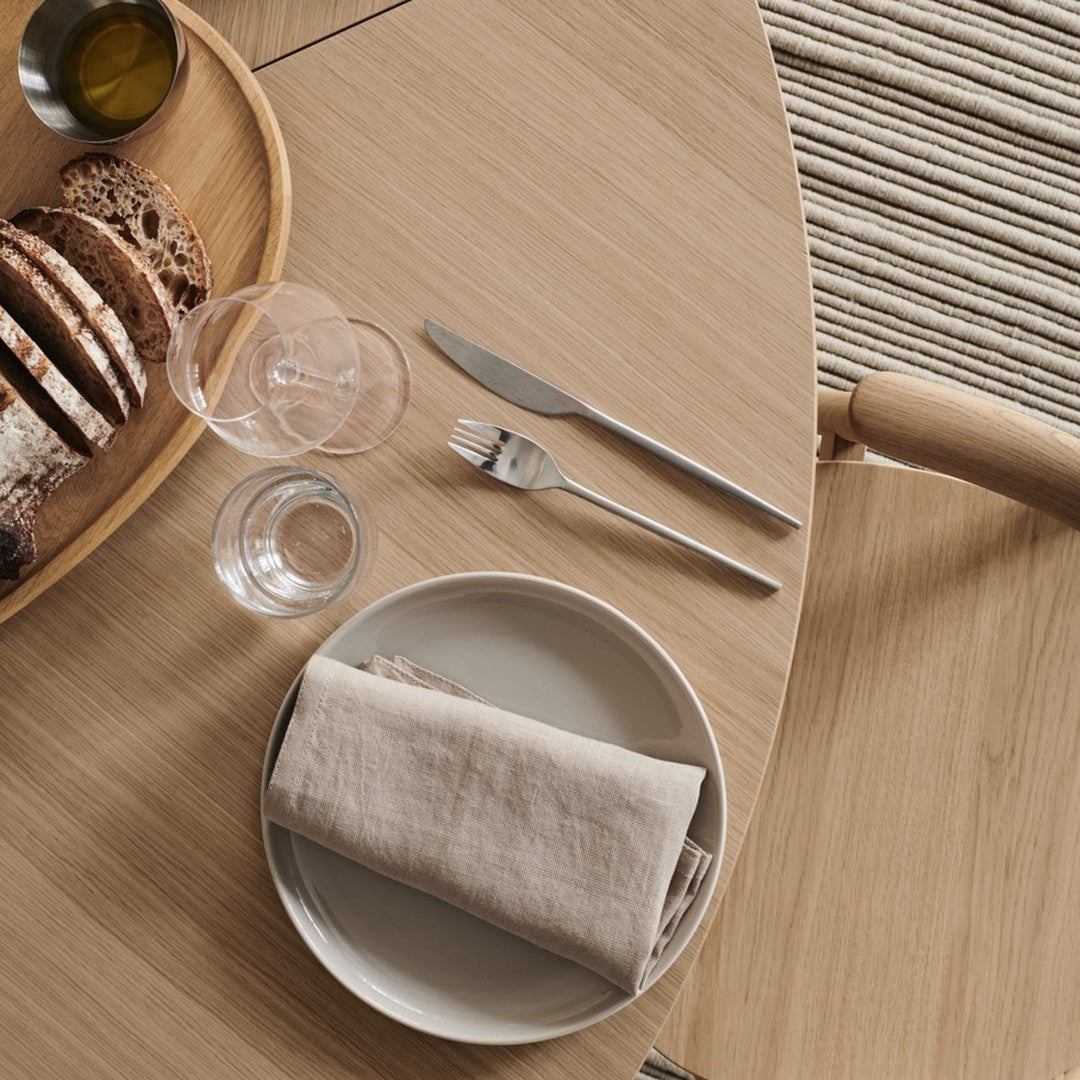 Minimalist table setting featuring earthy tones, soft grey napkin, sleek silver cutlery, and a textured wooden surface.