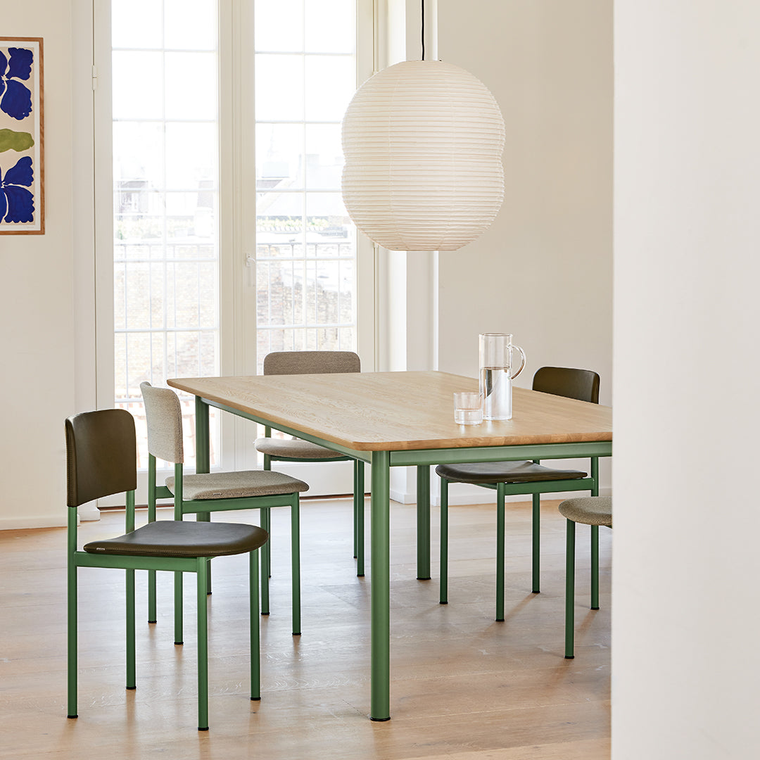 Light wood dining table with green metal legs, paired with black and white chairs in a bright, airy setting.
