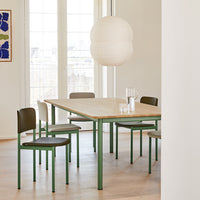 Light wood dining table with green metal legs, paired with black and white chairs in a bright, airy setting.