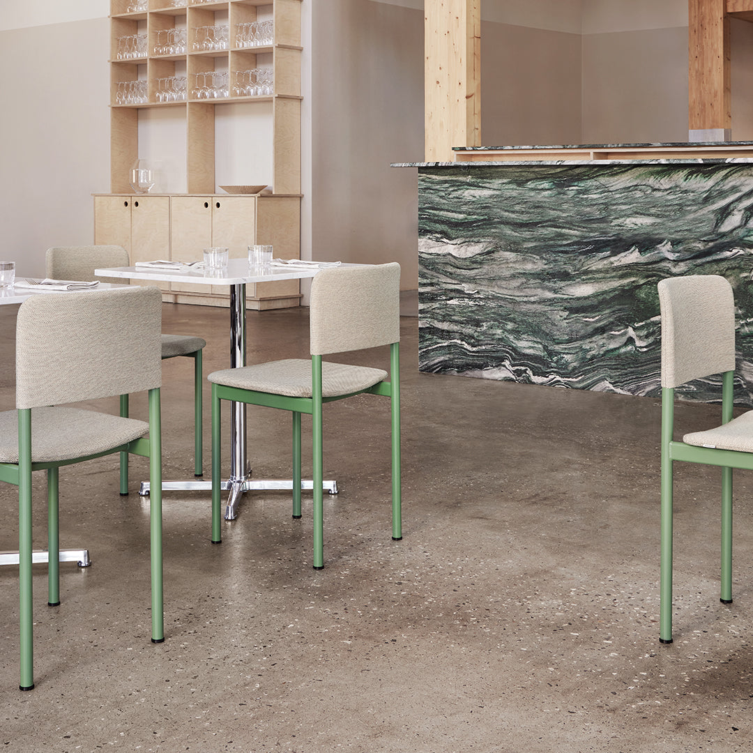 Light gray upholstered chairs with mint green legs beside a textured, dark green and white marbled bar.