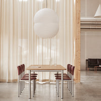 Scandi-style dining set with light wooden table, deep red chairs, and a round white pendant light against neutral curtains.