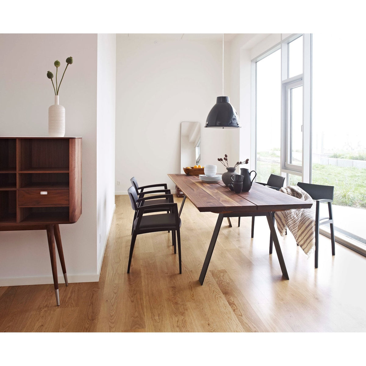 Modern dining room featuring light wood flooring, dark wooden table, black chairs, and neutral decor accents.