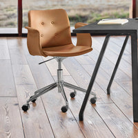Brown upholstered chair with button details and chrome base, set on a wooden floor next to a black table.