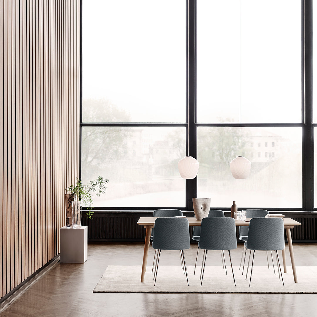 Modern dining space featuring blue chairs, light wood accents, and a neutral rug against a backdrop of large windows.