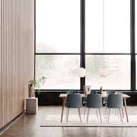Modern dining space featuring blue chairs, light wood accents, and a neutral rug against a backdrop of large windows.