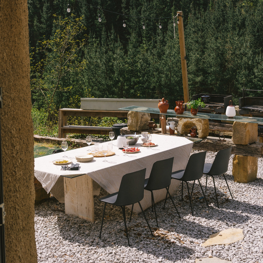 Rustic outdoor dining setup featuring a neutral tablecloth and sleek black chairs on a pebbled surface.