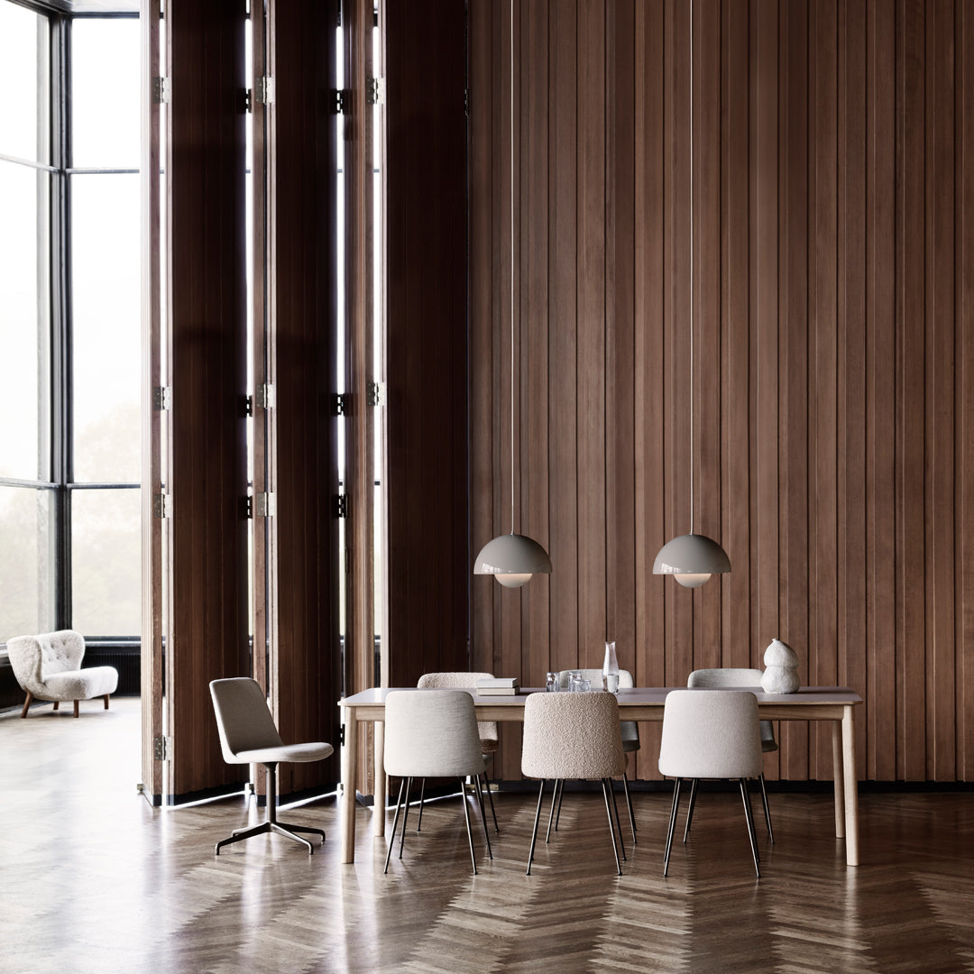 Modern dining room featuring light gray chairs, a wooden table, and patterned herringbone floors with warm wood tones.