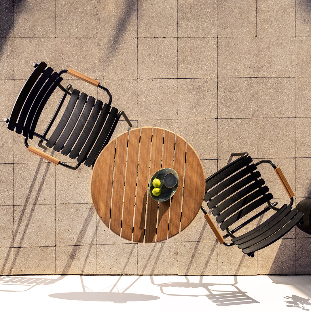 Black slatted chairs paired with a round wooden table, set on a light gray tiled surface. Perfect for outdoor living.