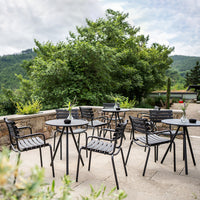 Black outdoor dining furniture with striped patterns, set against a lush green backdrop and cloudy sky.