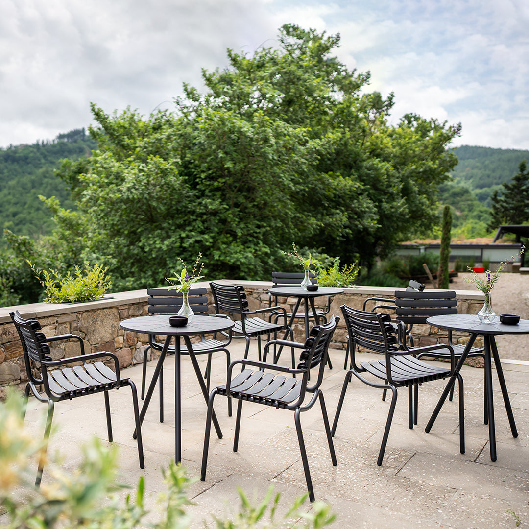 Black outdoor dining furniture with striped patterns, set against a lush green backdrop and cloudy sky.