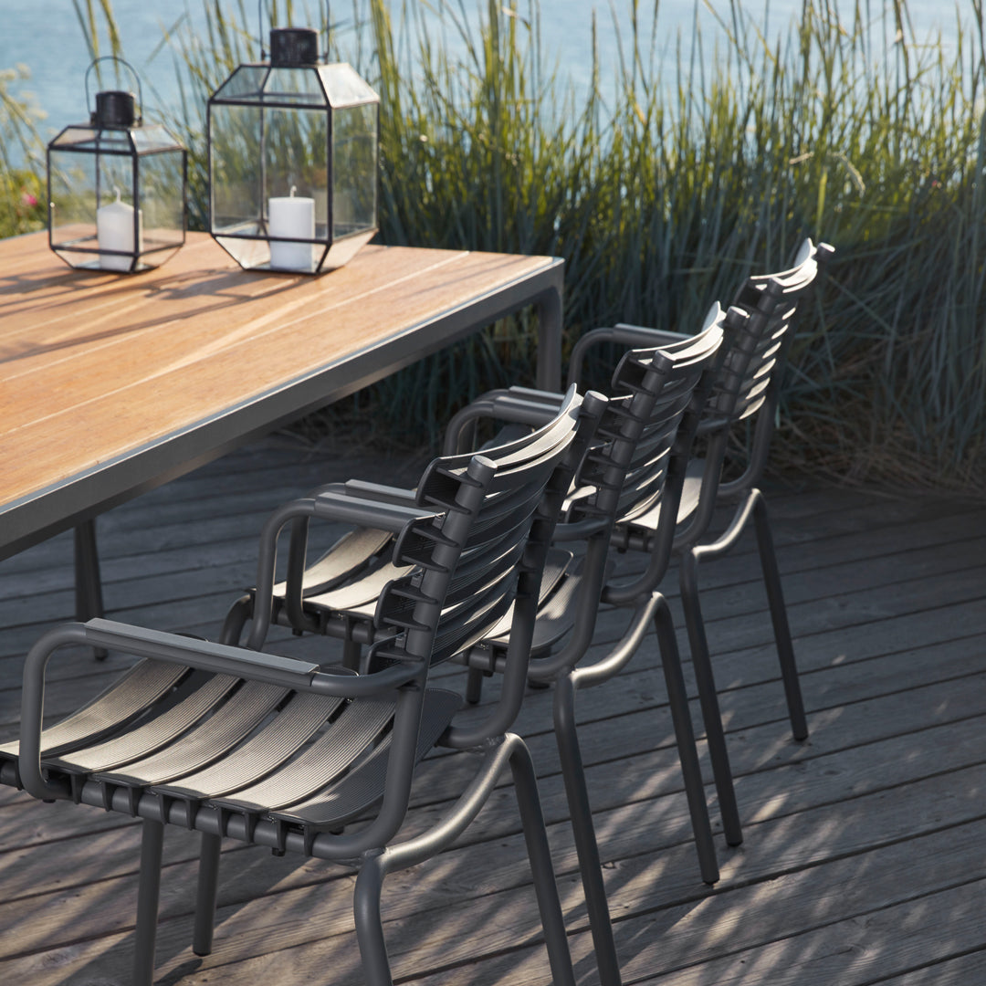 Contemporary black patio chairs with light wood table, set against lush greenery and a serene water backdrop.