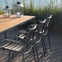 Contemporary black patio chairs with light wood table, set against lush greenery and a serene water backdrop.