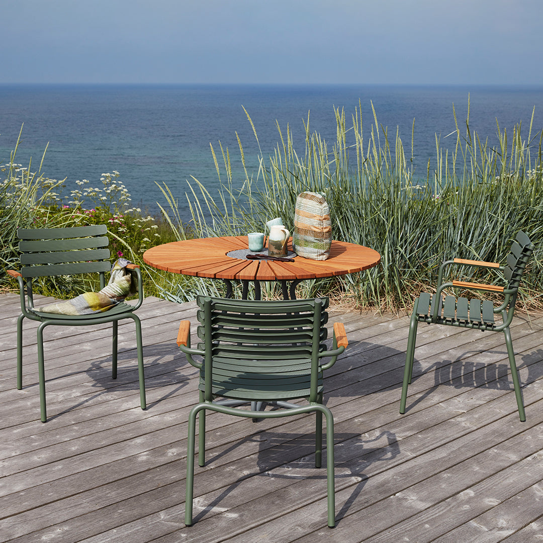 "Coastal dining set with green chairs, a round wooden table, and patterned accessories against a serene ocean backdrop."