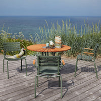 "Coastal dining set with green chairs, a round wooden table, and patterned accessories against a serene ocean backdrop."