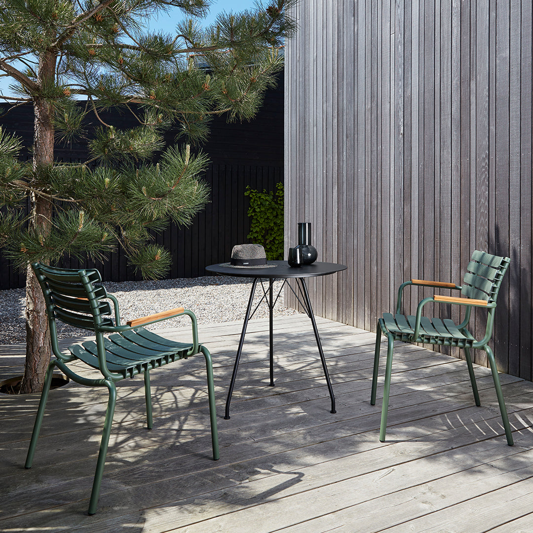 Two green striped chairs and a black round table set against a wooden deck and greenery.