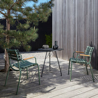Two green striped chairs and a black round table set against a wooden deck and greenery.
