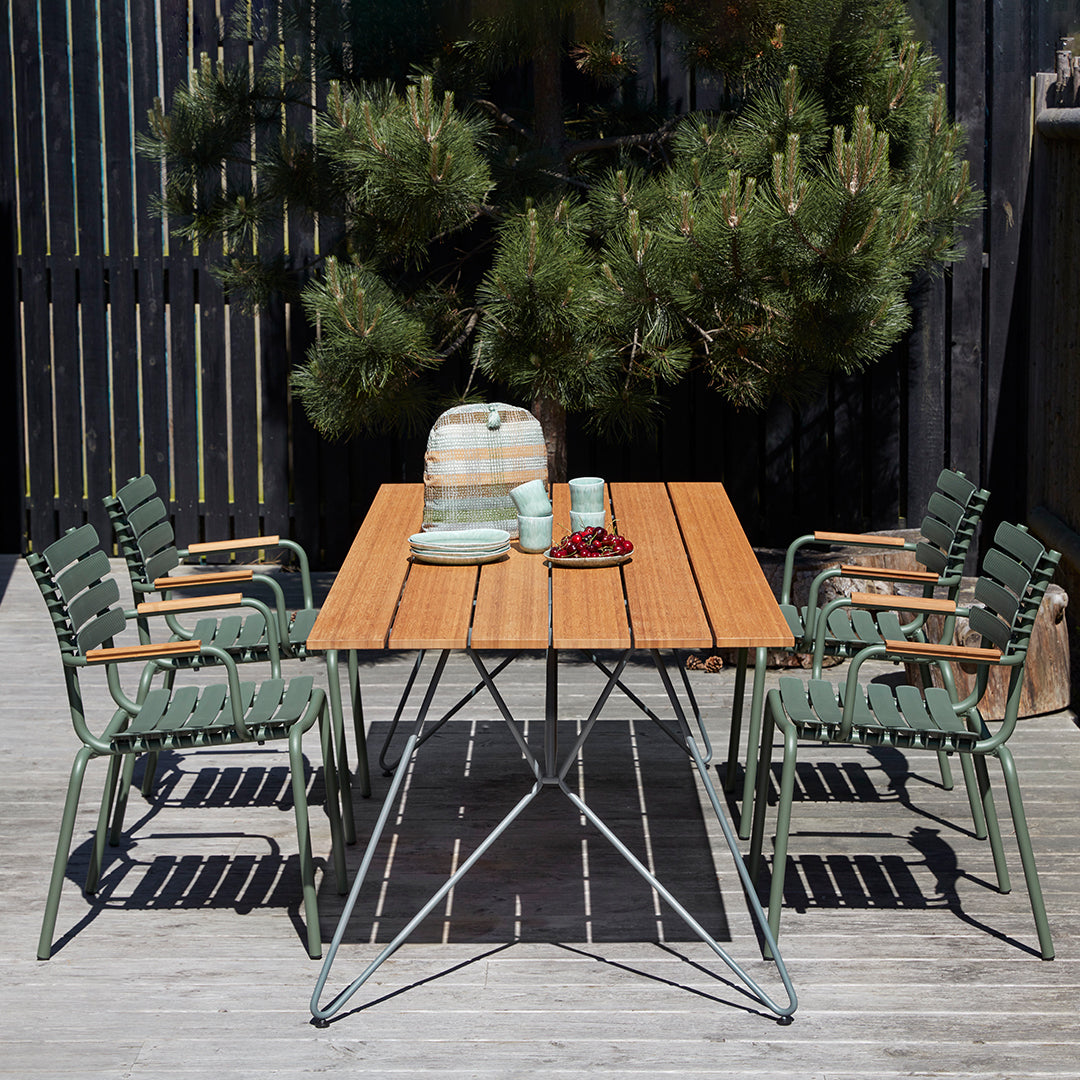 "Outdoor dining set with a natural wood table and green striped chairs, complementing a serene garden backdrop."