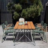 "Outdoor dining set with a natural wood table and green striped chairs, complementing a serene garden backdrop."