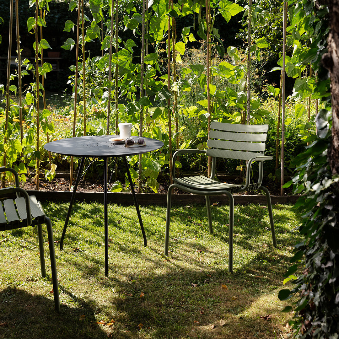 "Green striped chairs and round black table set in a lush garden surrounded by vibrant green plants."