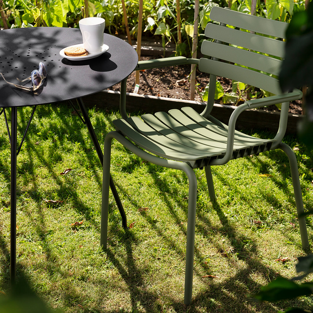 Green striped chair alongside a sleek black round table in a sunlit garden setting.