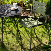 Green striped chair alongside a sleek black round table in a sunlit garden setting.