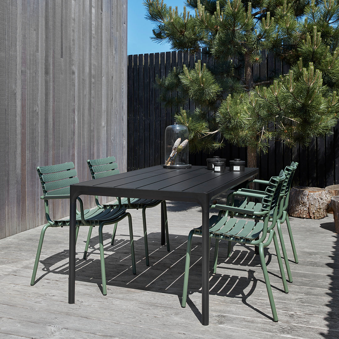 Modern outdoor dining set featuring a black rectangular table and six green metal chairs, set against a natural backdrop.