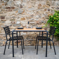Black metal dining set with wooden top, featuring a natural finish and sleek lines, against a rustic stone wall backdrop.