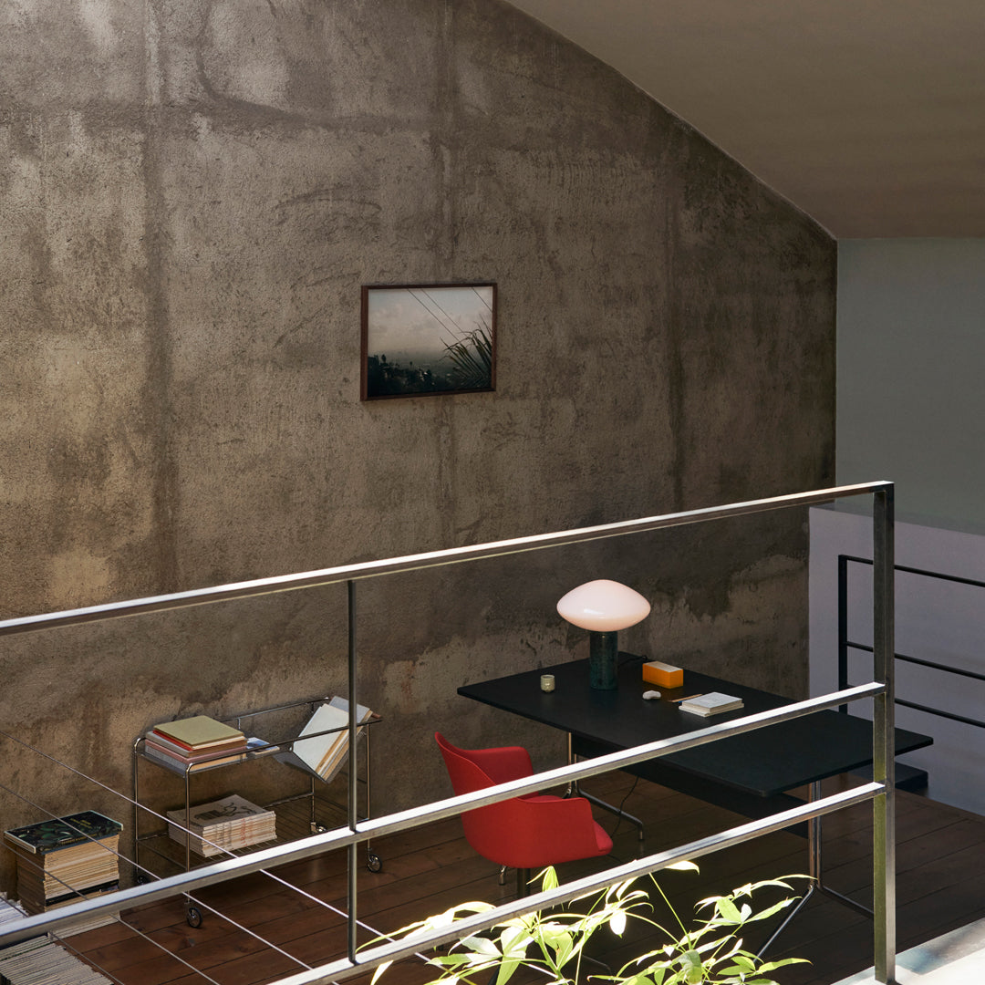 Modern interior featuring a red chair, black desk, and concrete wall, complemented by neutral tones and soft lighting.