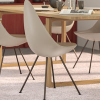 Beige dining chair with smooth curves and black metal legs, set against a warm-toned modern dining room backdrop.