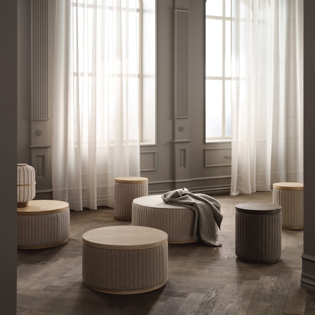 Neutral-toned round poufs with subtle ribbed patterns in a softly lit room with sheer white curtains.