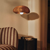 Woven brown pendant light hanging above a striped sofa in neutral tones, casting soft shadows on the wall.
