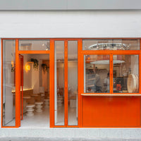 Bright orange storefront with large glass windows, featuring minimalistic design and light neutral interior elements.