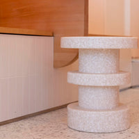 Textured white three-tiered side table with a minimalist design, set against light wood and cream background.