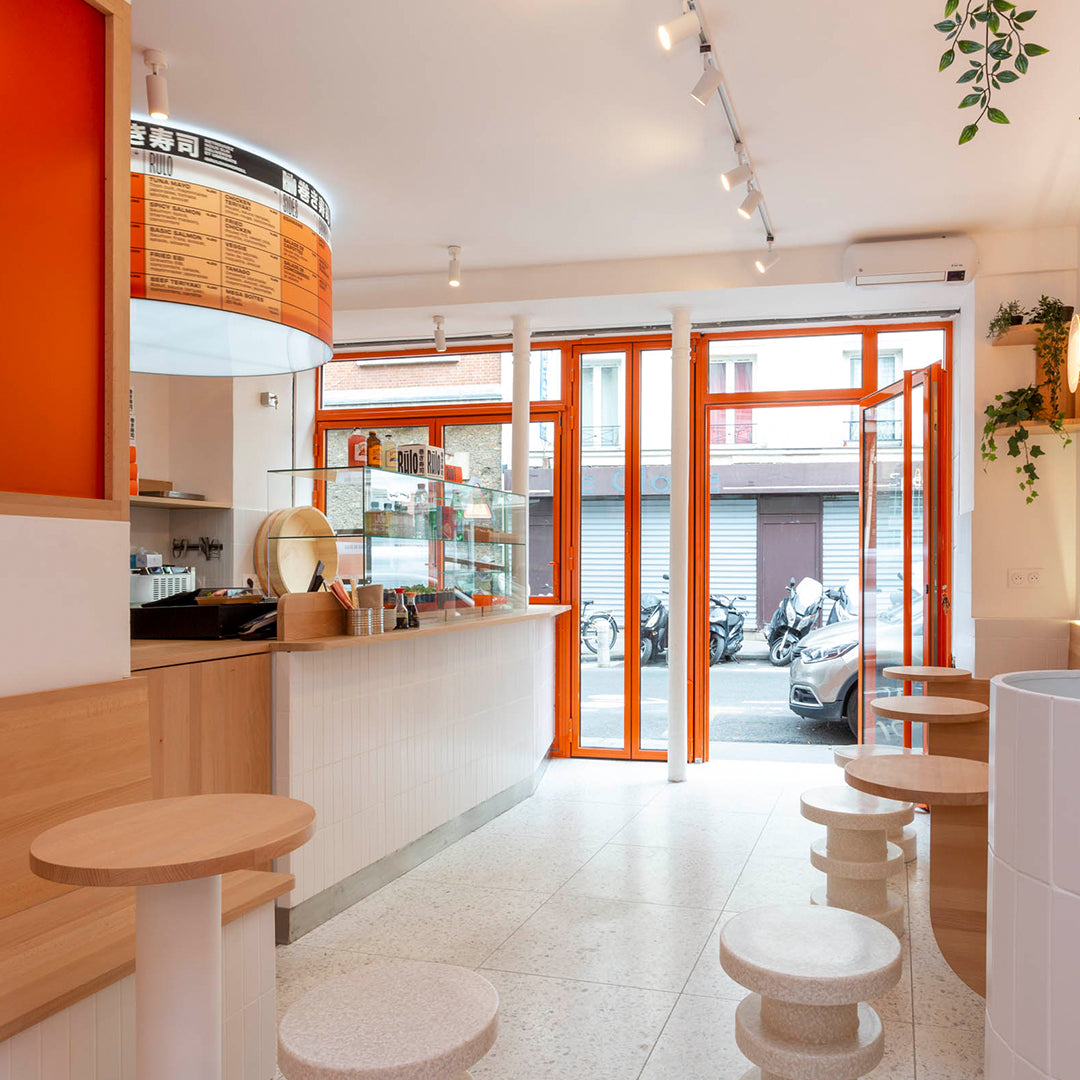 Bright orange accents and natural wood tones create a vibrant, inviting café atmosphere with light, minimalist patterns.