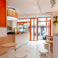 Bright orange accents and natural wood tones create a vibrant, inviting café atmosphere with light, minimalist patterns.